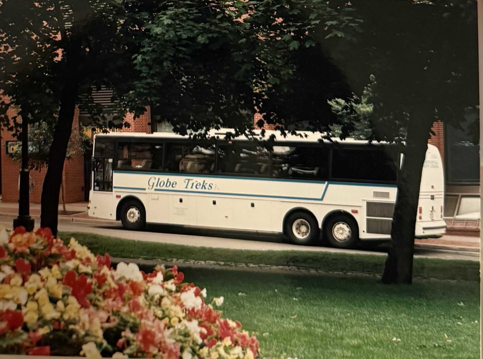A Globe Treks motorcoach parked under trees beside a flowerbed.